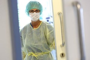 Krankenhaus-Mitarbeiterin in gelber Schutzkleidung mit Mund-Nasen-Schutz